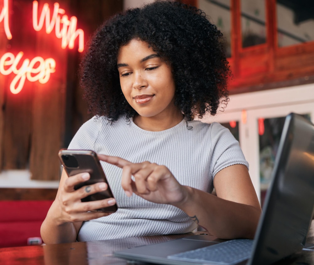 A woman on her phone in a cafe sending text messages with her new text marketing platform.